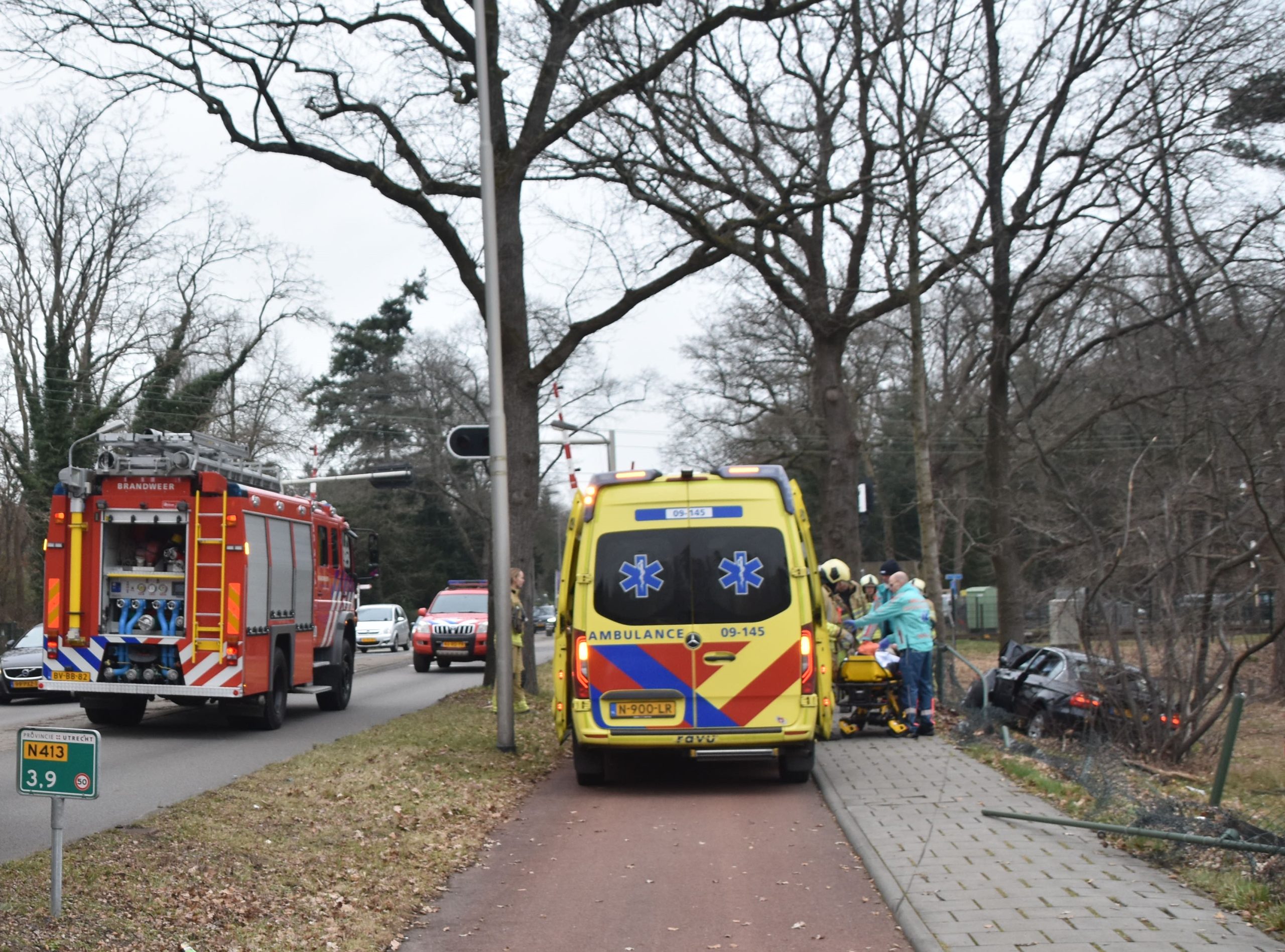 Auto dwars door hek tegen boom naast de weg
